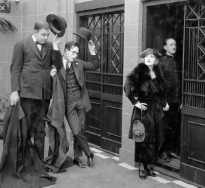 Men tipping hats at woman going into elevator, from the John Lloyd film High and Dizzy, 1920.